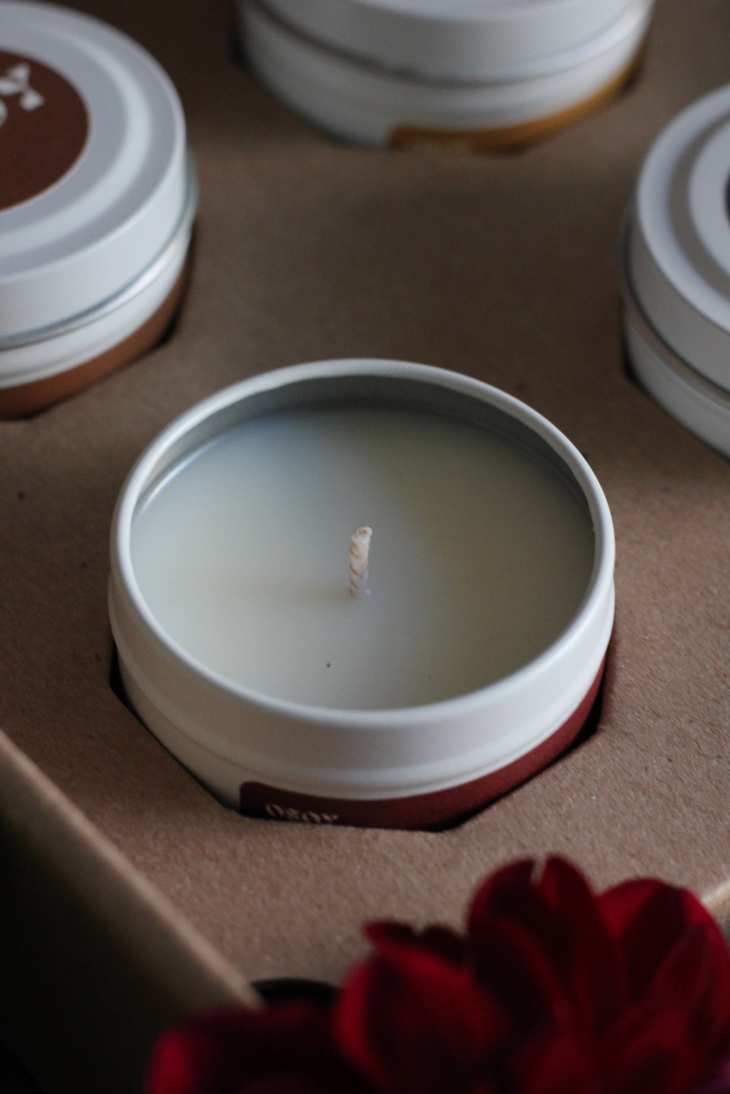 Close-up of a lit candle in a white container with a red flower in the background