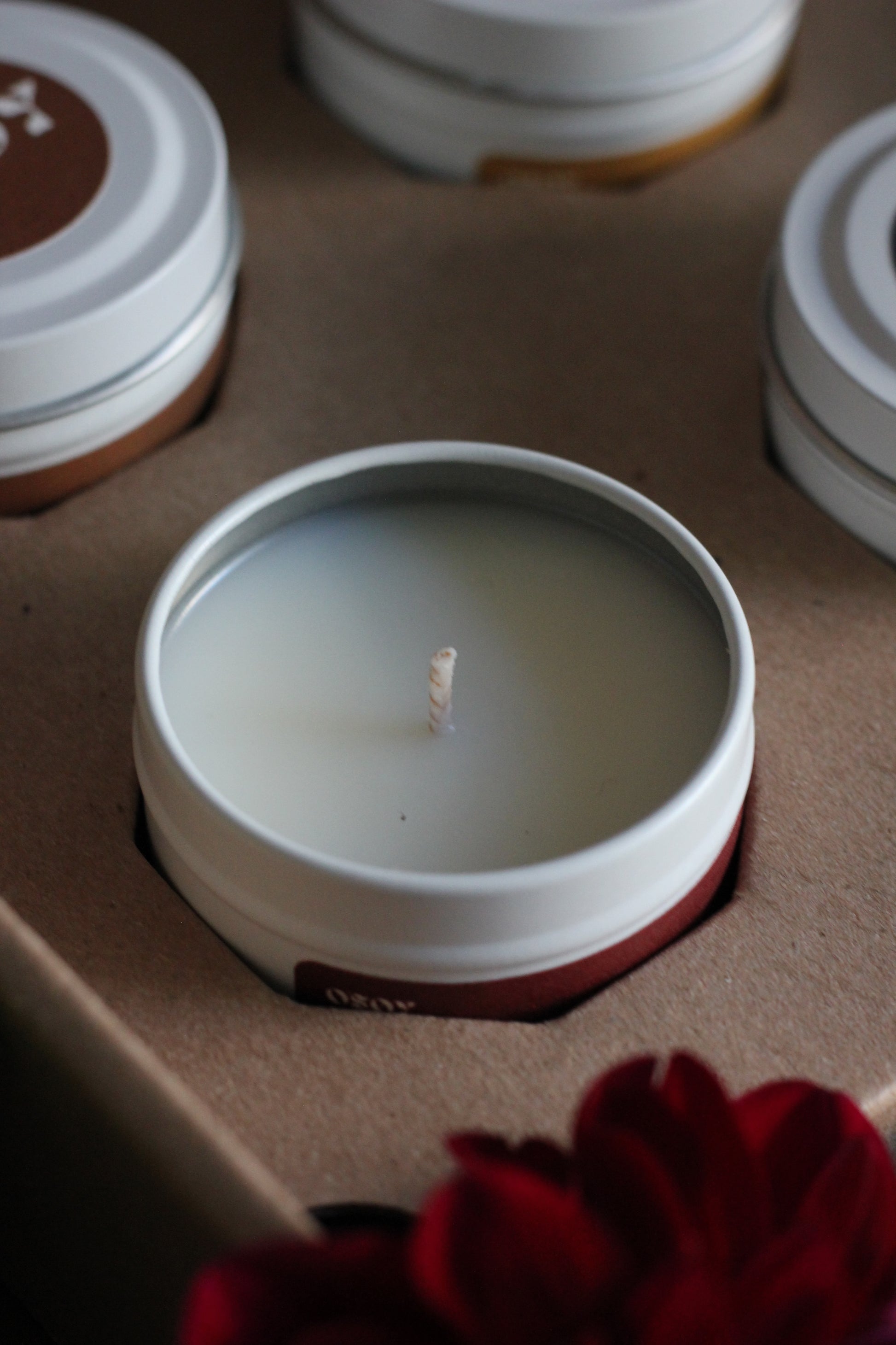 Close-up of a lit candle in a white container with a red flower in the background