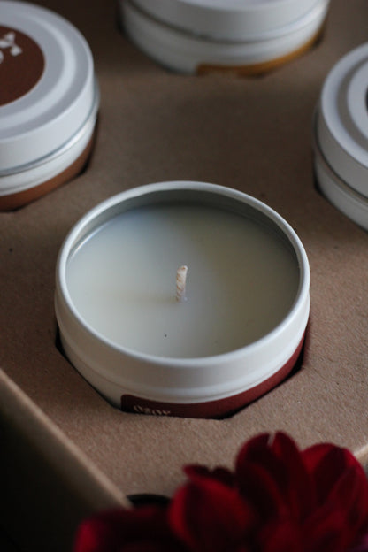 Close-up of a lit candle in a white container with a red flower in the background